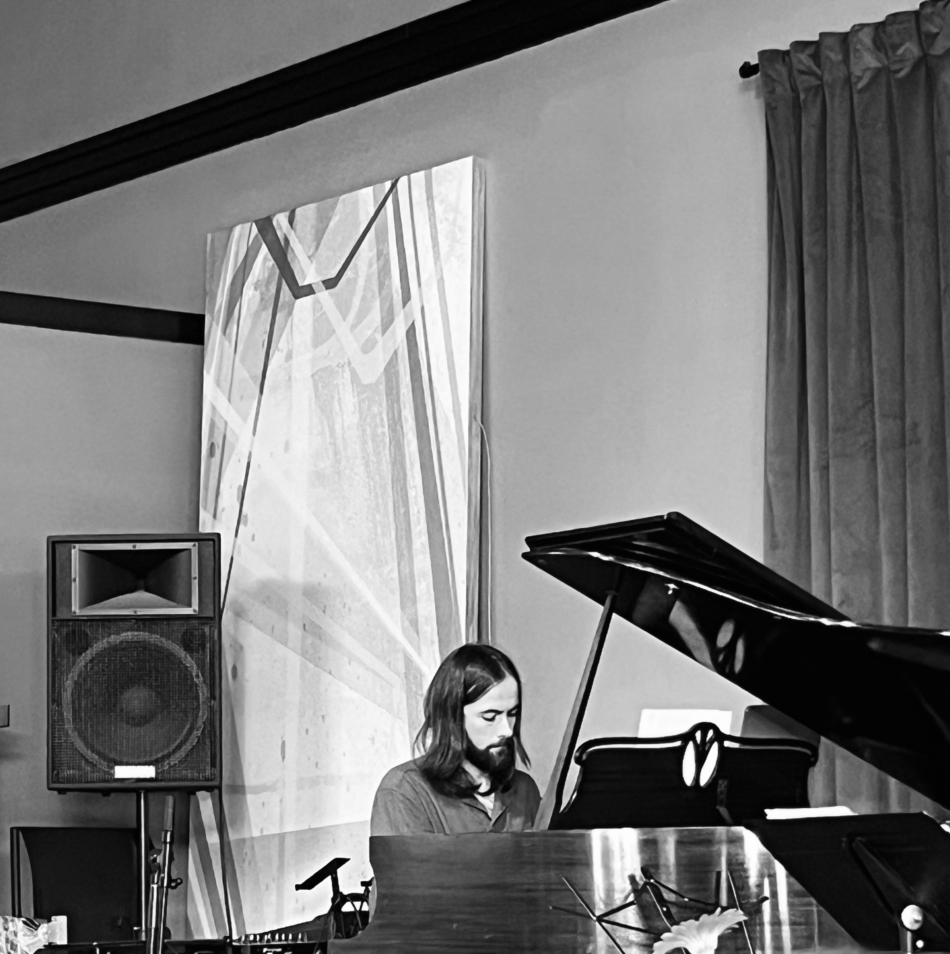 Andreas Garcia seated at a grand piano in a dim room, photographed in black and white