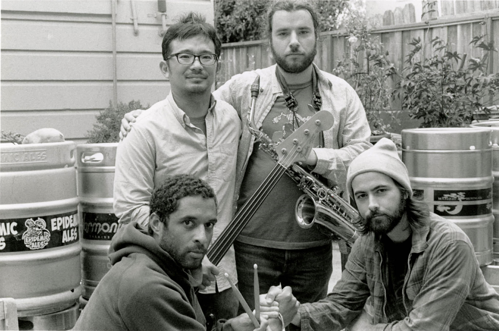 The Tree of Us quartet posed outdoors among beer kegs, one holding a saxophone