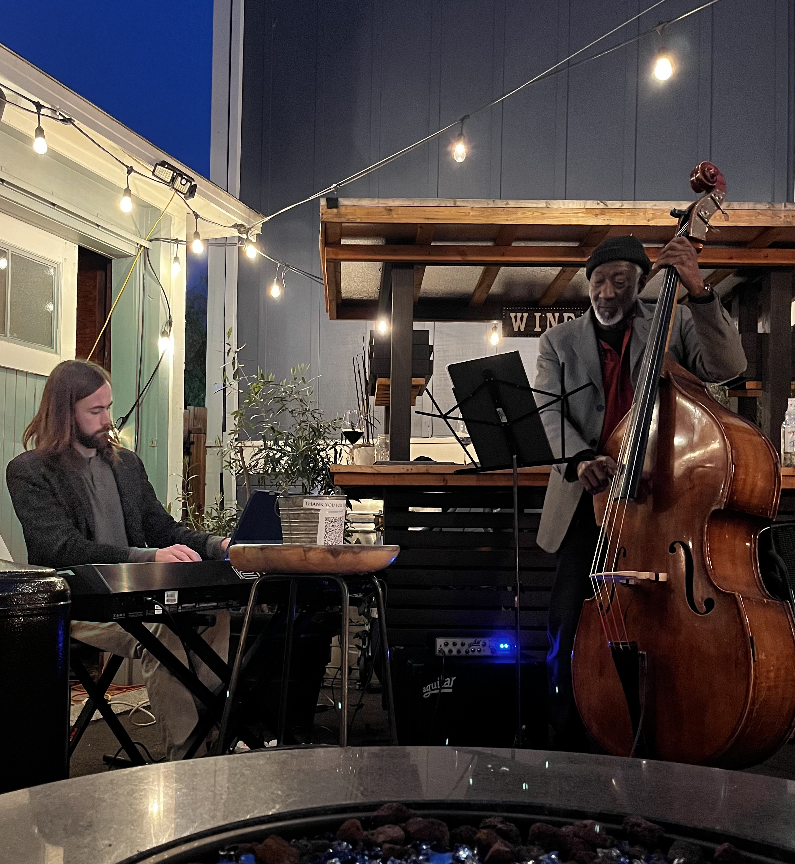Andreas Garcia at the keyboard alongside a bassist, playing an outdoor evening set under string lights